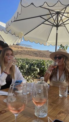 two women sitting at a table with wine glasses in front of them and an umbrella