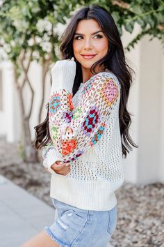 a beautiful woman posing for the camera wearing shorts and a sweater with crochet on it