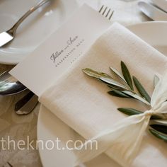 an elegant place setting with napkins, silverware and olive leaves on the table