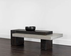 a black bowl sitting on top of a wooden table next to a white wall and hardwood floor