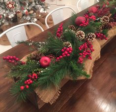 a wooden table topped with pine cones and red balls covered in greenery on top of burlap