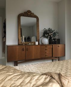 a bedroom with a bed, mirror and vase on the dresser in front of it