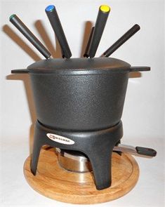 a black fonding pot with six different colored spoons in it on a wooden stand