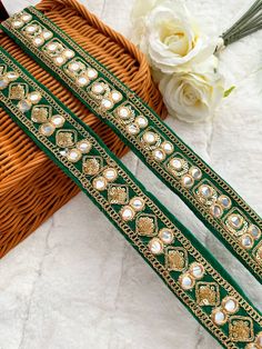 two pieces of green and gold colored thread with pearls on the ends, sitting next to a basket