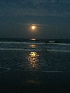 the moon is setting over the ocean with waves