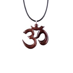 "This wooden Om pendant is hand carved in Cocobolo, an exotic hardwood that originates from Mexico, a wood highly diverse in colors and patterns, making this wearable art pendant unique and one of a kind. This particular exotic wood tends to darken over time, therefore by the time you will receive this pendant the wood might have settled into darker reddish-brown tones. The pendant is sealed with multiple layers of glossy wood lacquer that add a lot of shine to the piece.  - The pendant measures approximately 1.25\" tall by 1.25\" wide (3.2cm by 3.2cm).  - The pendant comes with an 18-20\" (47-51cm) adjustable black Korea waxed cord with lobster clasp, ready to wear. The waxed cord has a shinny snakeskin like texture and is a great non-fraying alternative to leather. We have more hand carv Spiritual Carved Necklaces For Festivals, Spiritual Brown Carved Jewelry, Spiritual Brown Carved Necklace, Ohm Necklace, Brown Carved Amulet Necklaces, Om Pendant, Wooden Cross, Art Pendant, Wood Crosses