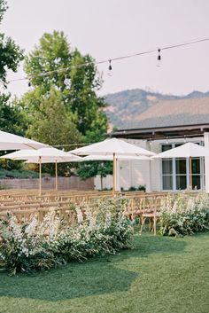 an outdoor wedding venue with tables and umbrellas in the grass, surrounded by greenery