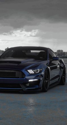 a black and blue mustang parked in front of a body of water on a cloudy day