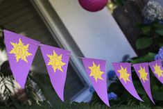 purple and yellow bunting with stars on it in front of some bushes, flowers and a pink ball