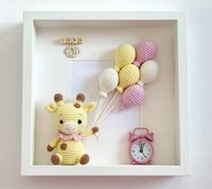 a crocheted giraffe holding balloons in a shadow box with a pink alarm clock