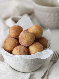 a white bowl filled with sugared donuts on top of a table next to a fork