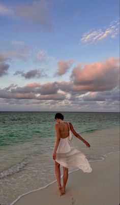 a woman is walking on the beach at sunset