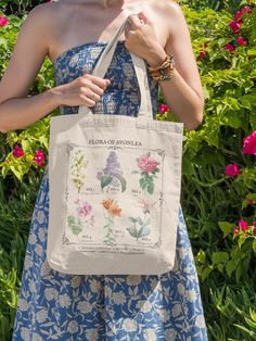 a woman in a blue dress is holding a white tote bag with flowers on it