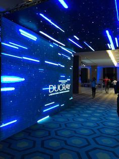 people are walking around in the lobby of a building with blue and white lights on it