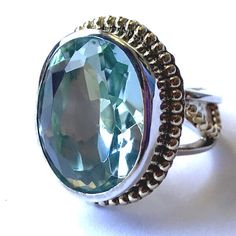 The beautiful sparkling green faceted stone in this ring is actually aqua colored recycled glass! It is an eye catching piece rimmed with Vermeil beads (Sterling Silver bathed in 22K Gold). The beading flows onto the open work band as well. The Face of this ring is 1" long and 3/4" wide. The band is 10mm and tapers to 5mm and has been left open to allow gentle resizing up to one ring size larger. It is being sold directly by the Offerings Sajen designers themselves! Green Oval Topaz Ring In Sterling Silver, Bohemian Green Rings With Gemstone Accents, Green Amethyst Jewelry With Gemstone Accents, Faceted Oval Rings For Jewelry Making, Faceted May Birthstone Ring Jewelry, Oval Faceted Rings For Jewelry Making, Green Blue Topaz Gemstone Rings, Green Large Gemstones For Anniversary, Large Green Gemstones For Anniversary