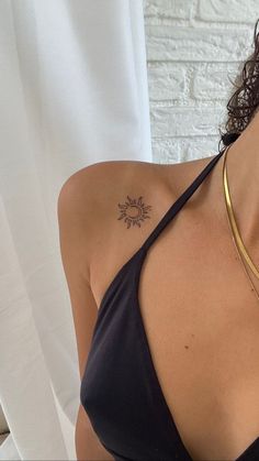 a woman with a sun tattoo on her chest wearing a black top and gold necklace