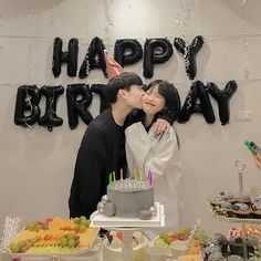 a man and woman kissing in front of a happy birthday sign with cupcakes