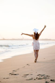 a woman is walking on the beach with her arms spread out and an umbrella over her head