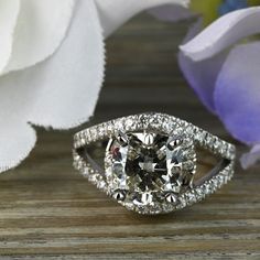 a fancy diamond ring sitting on top of a wooden table next to a purple flower