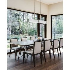 the dining room table is surrounded by white chairs and large windows that look out onto the woods