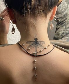 the back of a woman's neck with a dragonfly tattoo on her left side