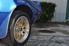 a blue sports car with gold rims parked in front of a white building on the street