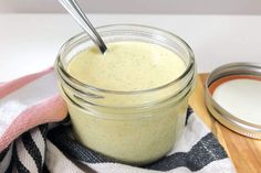 a glass jar filled with cream sitting on top of a wooden cutting board next to a spoon