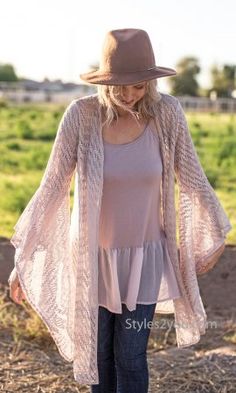 a woman wearing a brown hat and cardigan is standing in the dirt with her hands on her hips