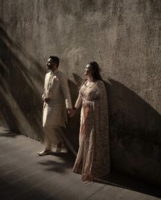 two people standing next to each other in front of a cement wall holding hands and looking up at the sky