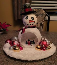 a snowman made out of glass sitting on top of a counter next to ornaments