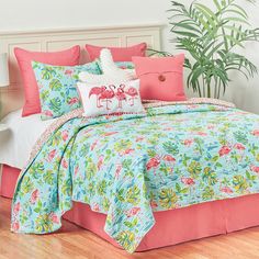 a bed with flamingos on it and pink pillows in the corner next to a potted plant