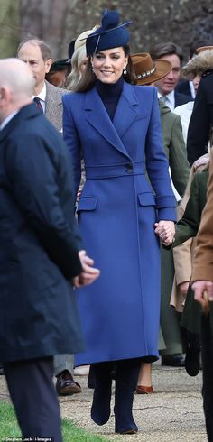 a woman in a blue coat and hat is walking with other people behind her on the sidewalk