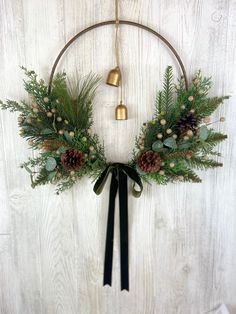 a wreath with pine cones, evergreen leaves and bells hanging on a white wooden wall