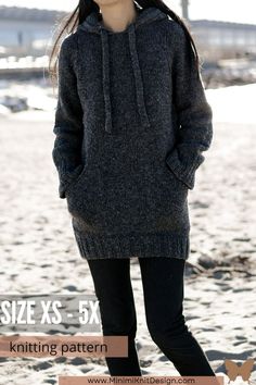 a woman standing on top of a sandy beach wearing a gray sweater and black pants