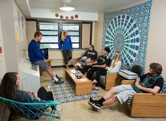 a group of young people sitting around each other in front of a wall with an art work on it