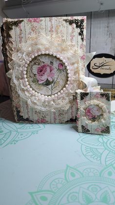 a table topped with an open book covered in lace and pink flowers on top of it