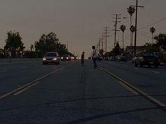 cars are driving down the street at dusk in this city area with palm trees and telephone poles