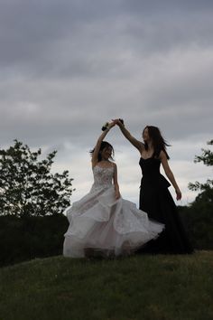 two women in dresses are standing on a hill and one is holding the other's hand