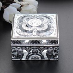 a silver box sitting on top of a black table next to flowers and a white flower