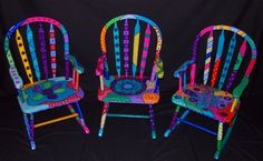 three brightly colored chairs sitting next to each other on a black background in front of a black backdrop