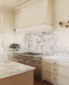 a white kitchen with marble counter tops and gold trim on the hood, cabinets and drawers