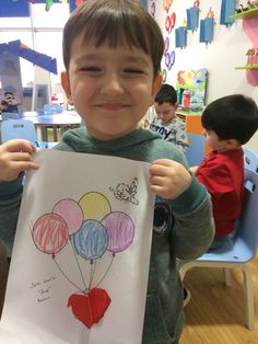 a young boy holding up a drawing with balloons on it