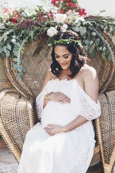 a pregnant woman sitting in a wicker chair with flowers on her head and wearing a white dress