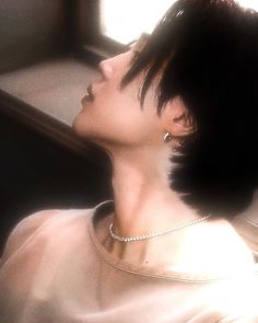 a woman with short black hair wearing a white shirt and diamond necklace looking up into the sky