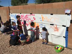 several children are painting on a wall outside