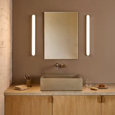 a bathroom sink with two mirrors above it and lights on the wall next to it