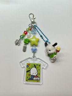 two key chains with charms attached to them on a white surface, one has a small dog and the other is a t - shirt