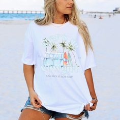 a woman standing on the beach wearing a white shirt