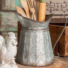 a metal container filled with wooden utensils on top of a table next to a chicken figurine