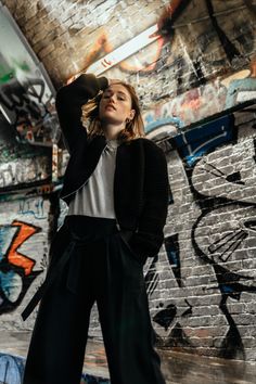 a woman standing in front of graffiti covered walls wearing black pants and a white t - shirt